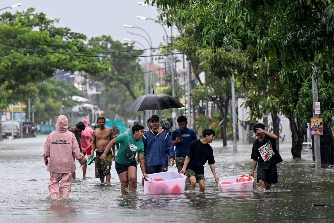 People move their belongings through the water on an inundated street amid floods following heavy rain at Legian Kuta near Denpasar on Indonesia's resort island of Bali on Feb 24, 2026. 
