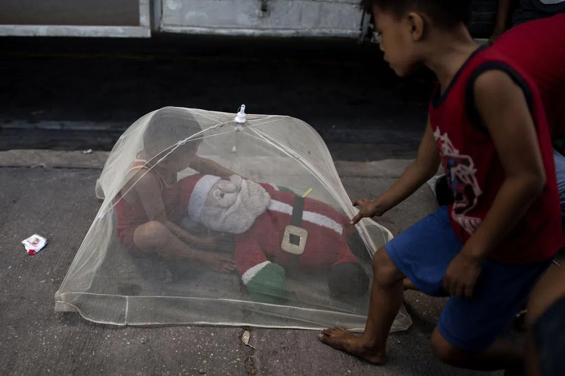 A boy underneath a mosquito net plays with a Santa Claus stuffed toy in Manila on Oct 13, 2018. 