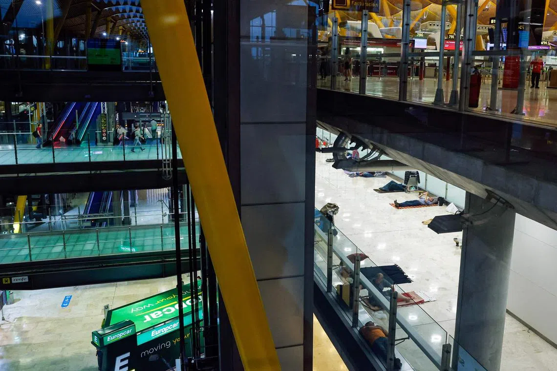 Passengers (TOP) make their way to flights as homeless people (BELOW) lay on the floor of Terminal 4 of the Adolfo Suarez Madrid-Barajas airport in Madrid, on May 28, 2025. New security measures recently announced to only allow people holding boarding passes to enter after 9 p.m. were implemented to deter ovrnight stays of hundreds of homeless people. The measure is the latest effort to address the rising number of people sleeping at Spain’s busiest airport — a situation thrust into the spotlight by images showing rows of people lying on the floor amid bags and shopping carts, sparking a blame game among government officials at various levels. (Photo by OSCAR DEL POZO / AFP)