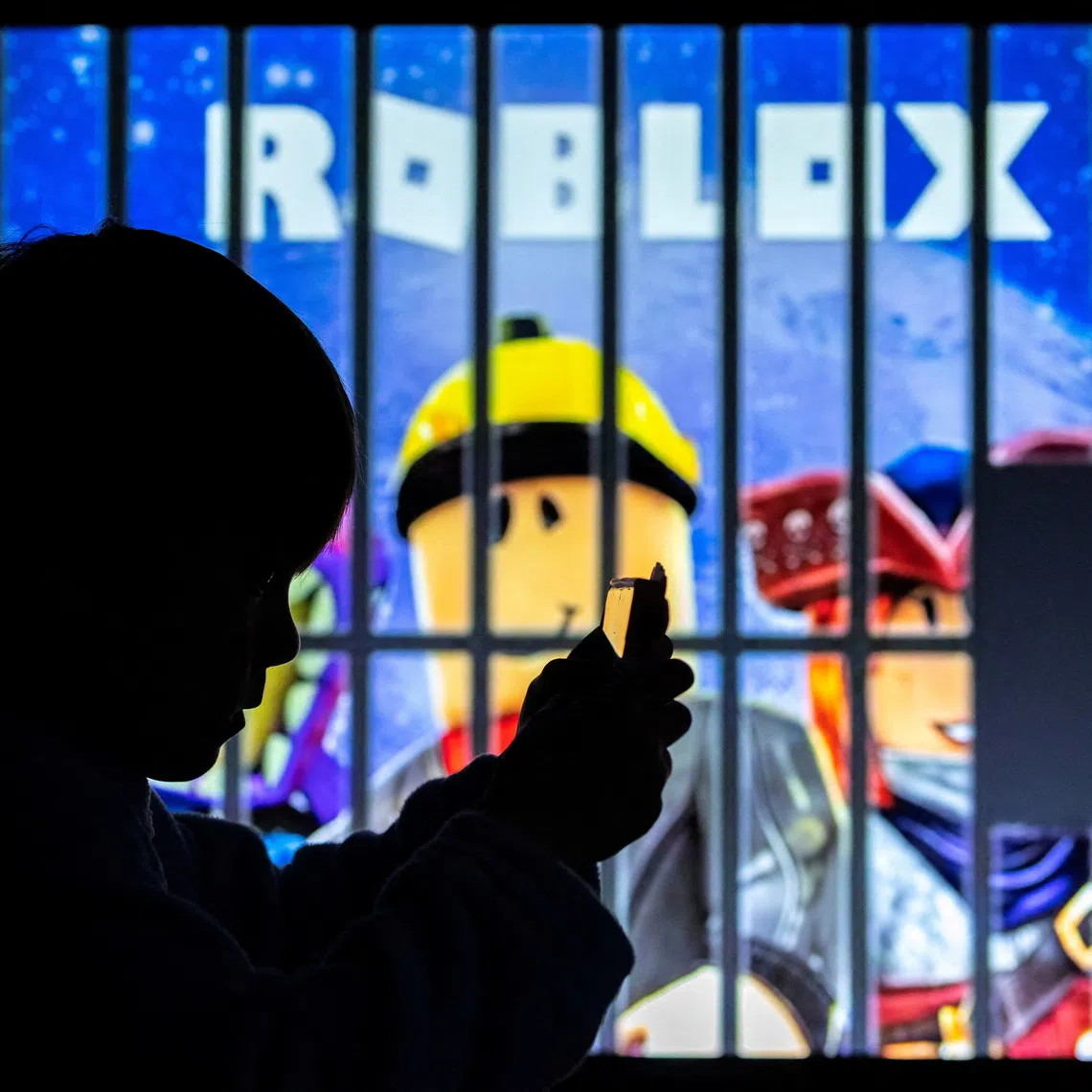 FILE PHOTO: A boy poses for a photo while holding a smartphone in front of a screen displaying characters of the U.S. children's video game Roblox, in this illustration taken December 8, 2025. REUTERS/Ramil Sitdikov/Illustration/File Photo