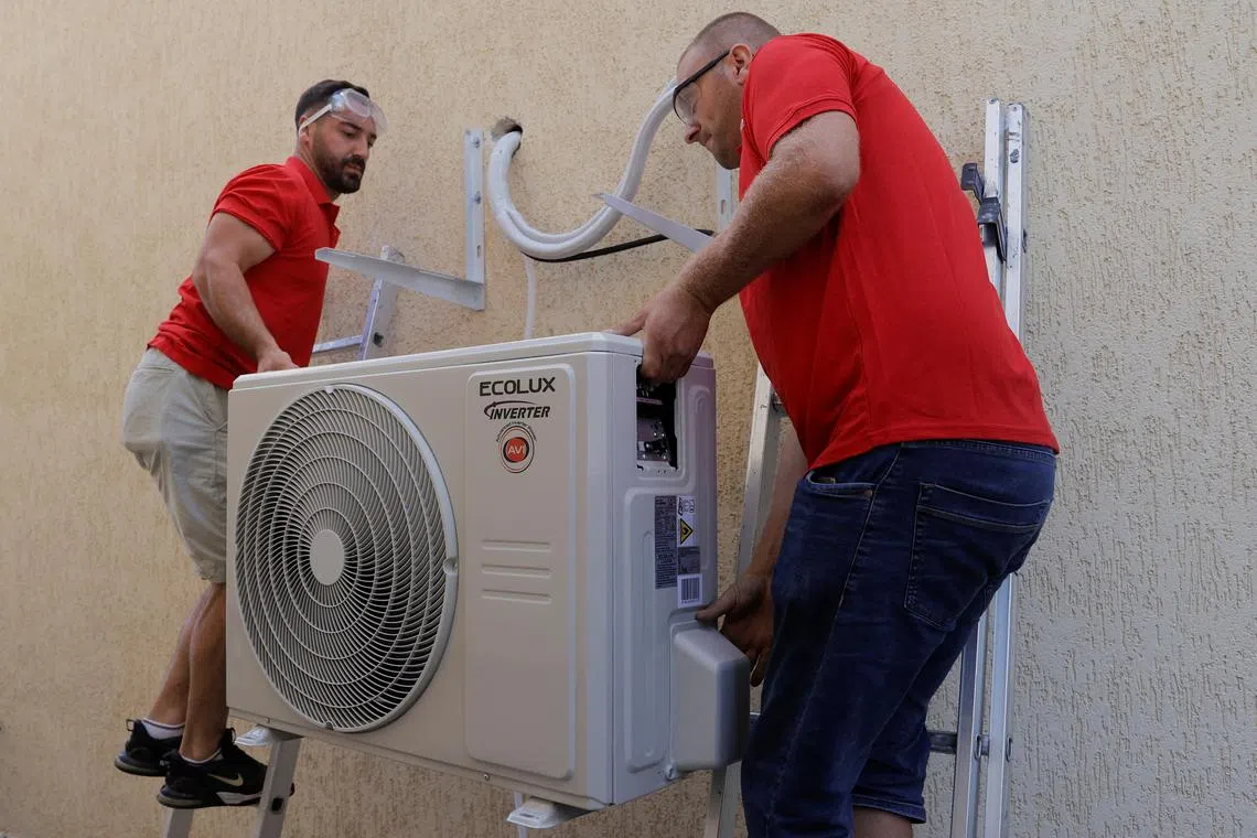 Workers mounting an air-conditioner unit at a house in Kosovo,  in July 2024.