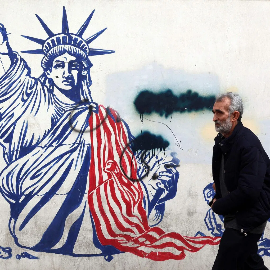 A man walks past a mural depicting the Statue of Liberty with is torch-bearing arm broken, painted on the outer walls of the former US embassy, in Tehran.