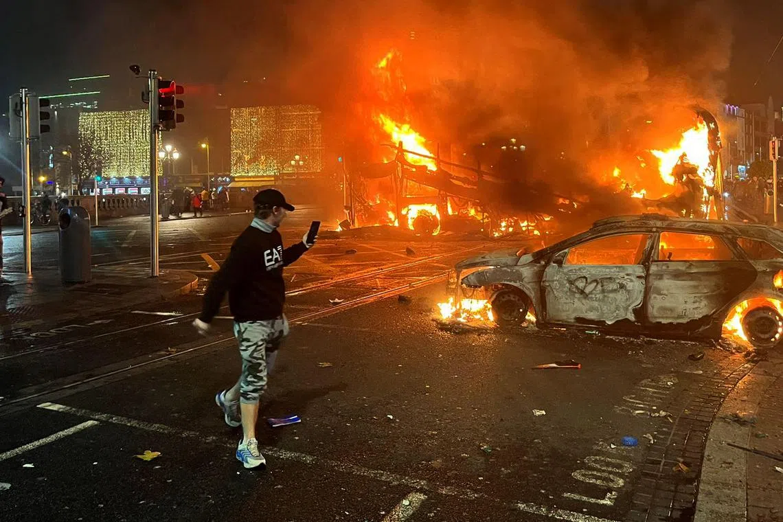 TOPSHOT - Flames rise from a car and a bus, set alight at the junction of Bachelors Walk and the O'Connell Bridge, in Dublin on November 23, 2023, as people took to the streets in protest following the stabbings earlier in the day. Protesters in Dublin on Thursday torched a car and fought police, an AFP journalist reported, after three children were injured in a suspected school stabbing that social media rumours attributed to a foreign national. (Photo by Peter MURPHY / AFP)