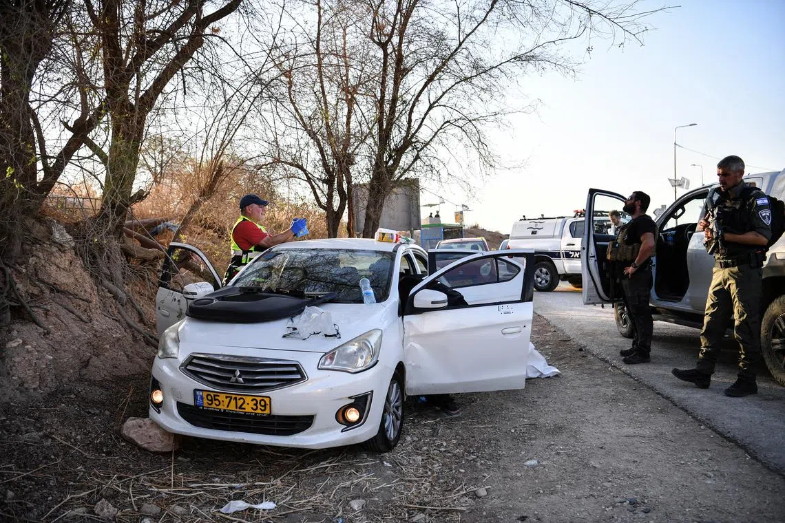 Israeli emergency services and soldiers stand next to a car with bullet holes at the scene of a suspected shooting attack in the West Bank.