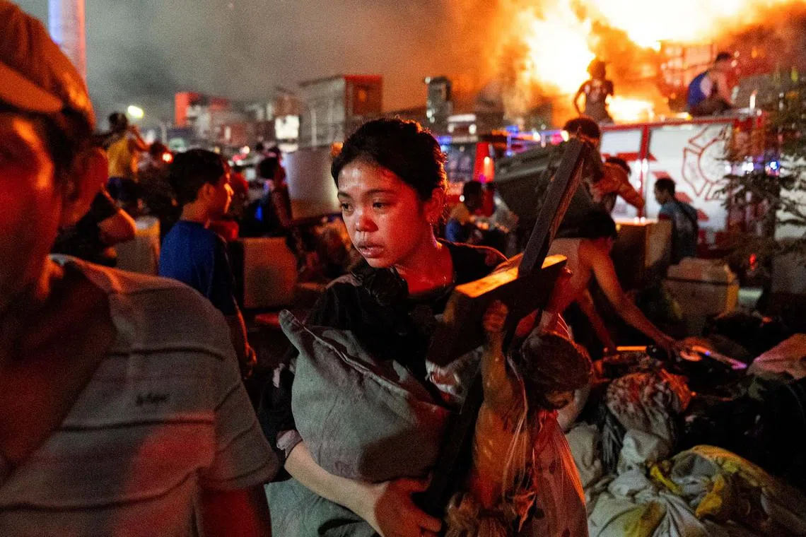 A woman carrying a crucifix as she escapes the fire at a residential area in Manila, Philippines, April 23, 2025. 