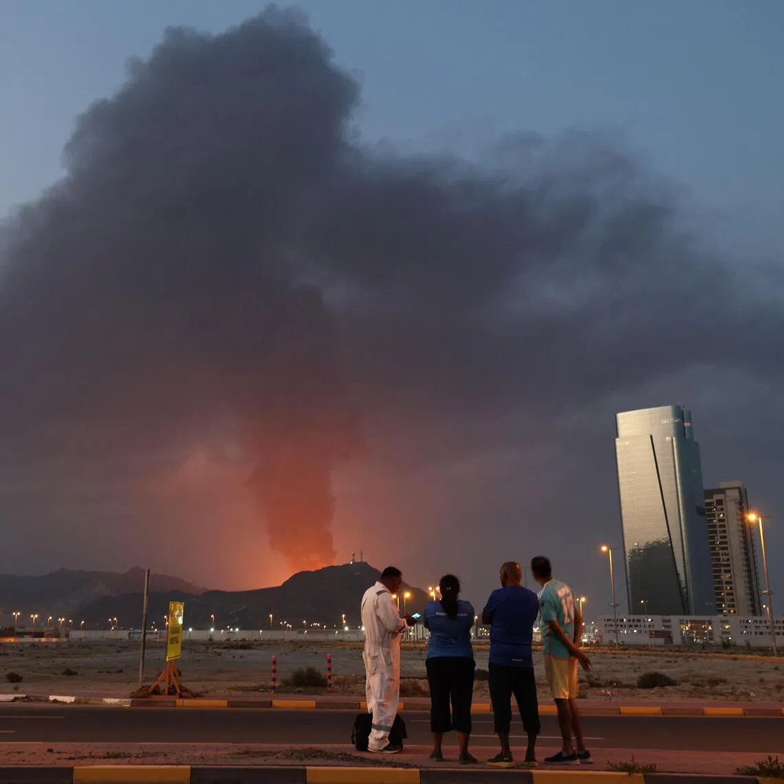 Foreign workers watch smoke rising from the UAE's Fujairah industrial zone on March 3, following an explosion.