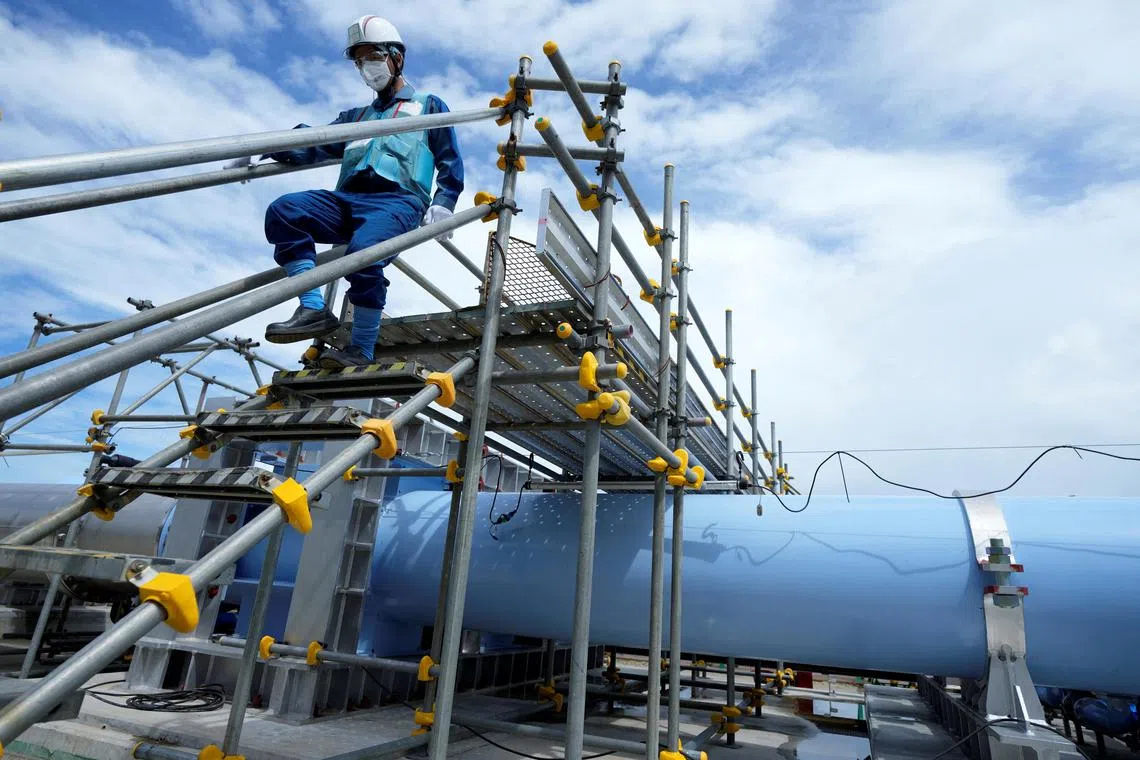 A Tepco employee walks near a blue pipeline that releases treated radioactive water to the sea from the Fukushima Daiichi nuclear power plant.