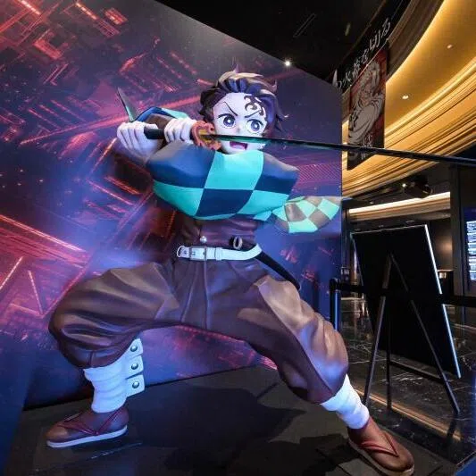 This photo taken on September 9, 2025 shows a woman walking past a statue of young swordsman Tanjiro Kamado (L), the title character in the Japanese anime film "Demon Slayer", on display at a cinema in the Ikebukuro area of Tokyo. "Demon Slayer" has set records, just like its predecessor in the series and other anime films, becoming Japan's fastest film to gross 10 billion yen (67 million USD). (