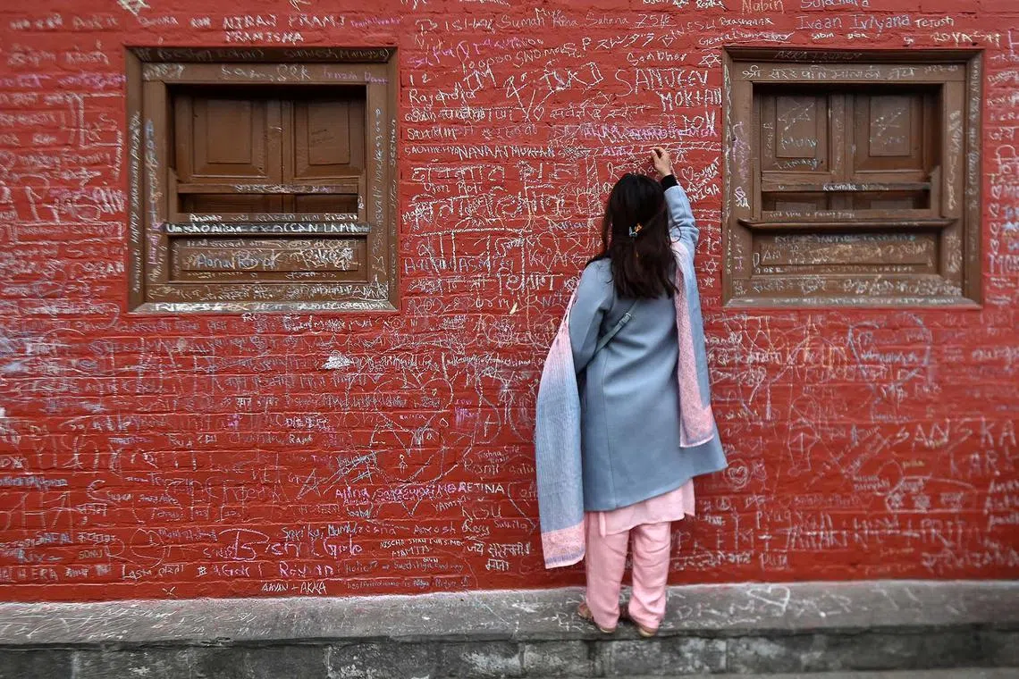 TOPSHOT - A devotee writes a message with chalk on a wall at the Saraswati temple on the occasion of the Hindu festival of 'Basanta Panchami', in Kathmandu on February 14, 2024. (Photo by PRAKASH MATHEMA / AFP)