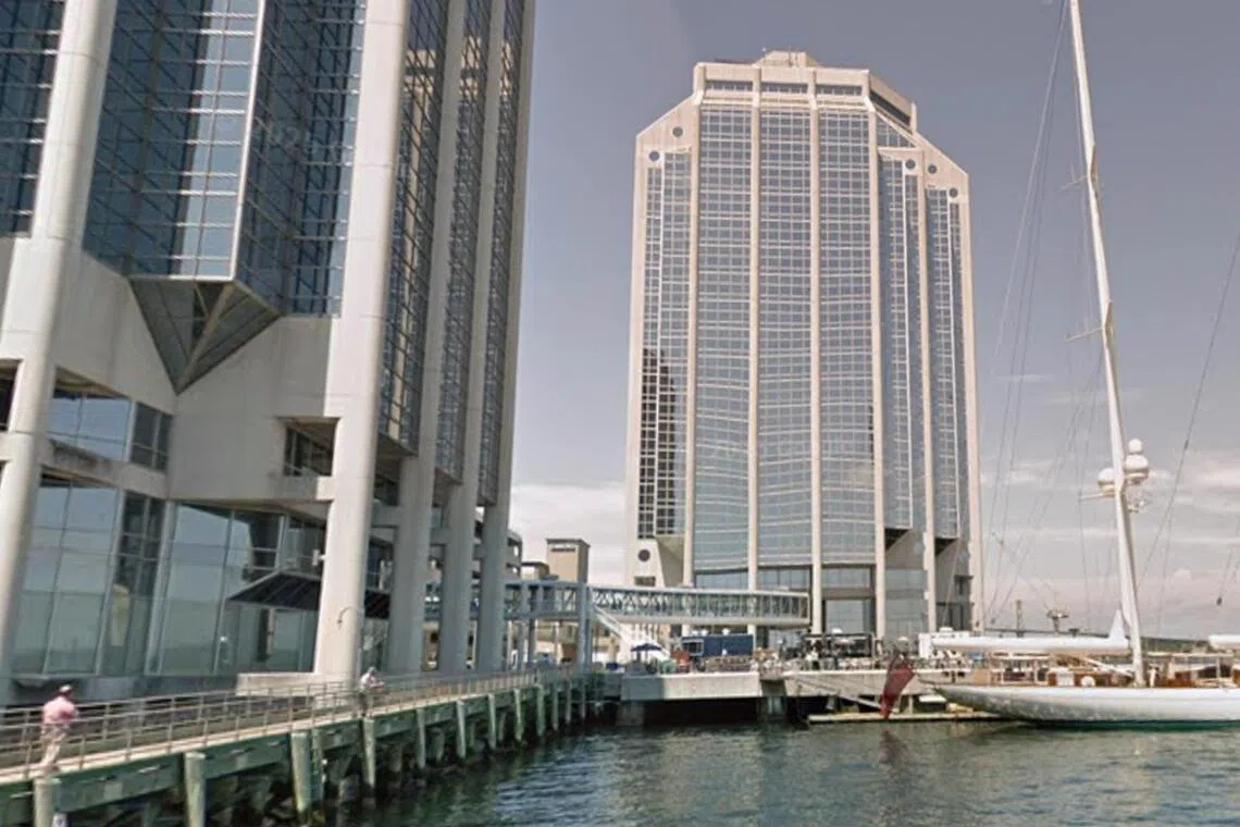 Two tall buildings stand near a marina with sailboats.