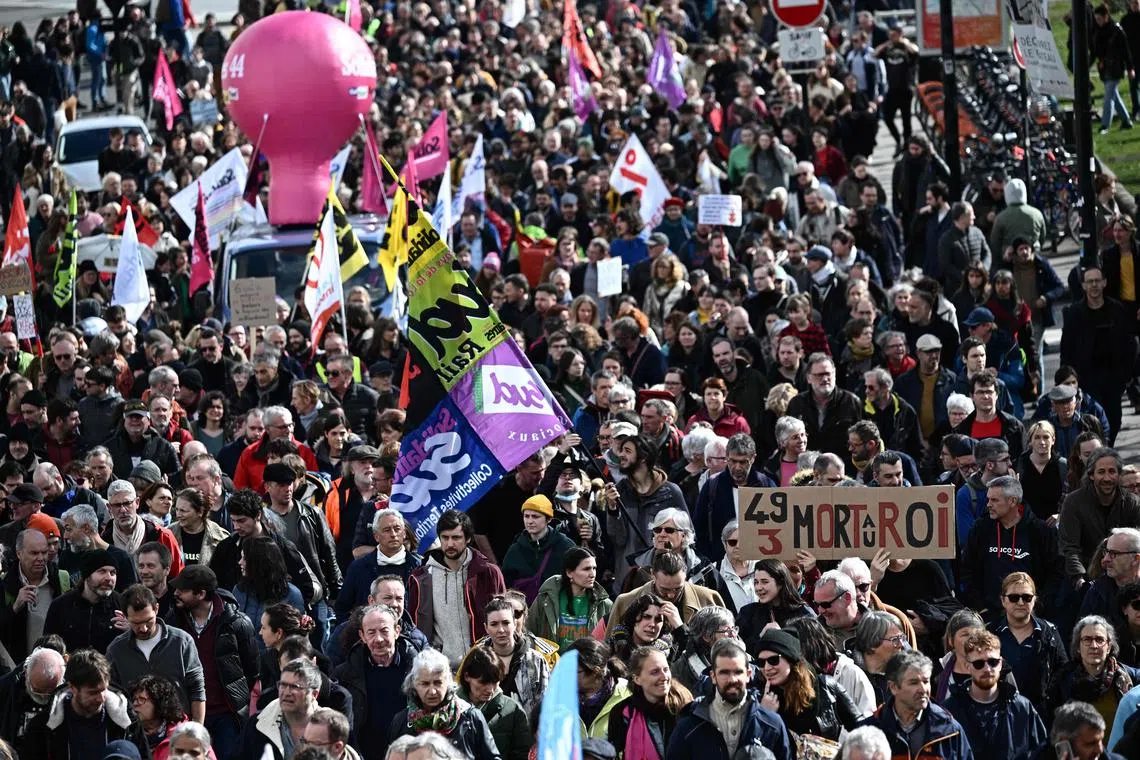 Protesters march holding a placard which reads as "49.3, Death to the king", during a demonstration in Nantes, western France, on March 18, 2023, two days after the French government pushed a pensions reform through parliament without a vote, using the article 49.3 of the constitution. - France on March 18 braced for a weekend of protests, after a second night of unrest sparked by the French president imposing without a parliament vote an unpopular pension overhaul, that includes raising the retirement age from 62 to 64. (Photo by LOIC VENANCE / AFP)