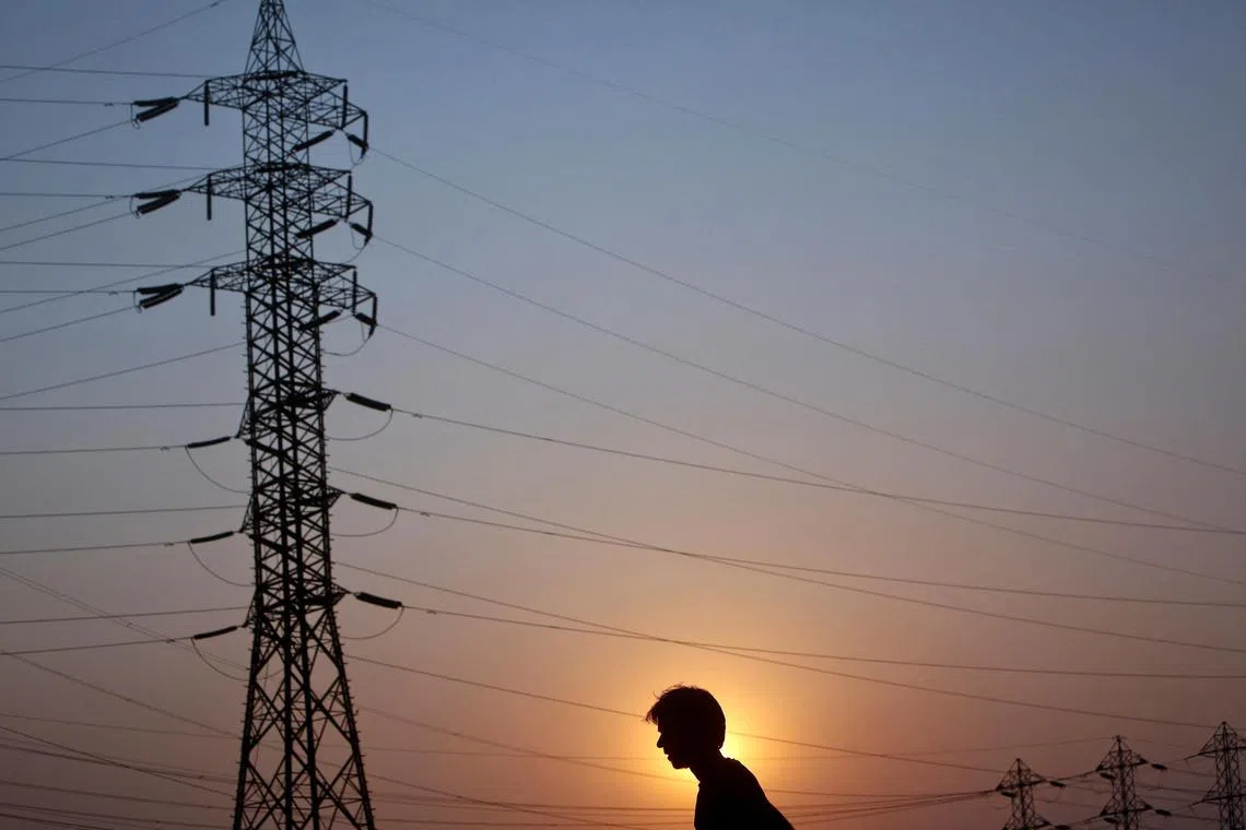 FILE PHOTO: A man walks under high-tension power lines on the outskirts of Mumbai February 13, 2013. REUTERS/Vivek Prakash/File Photo