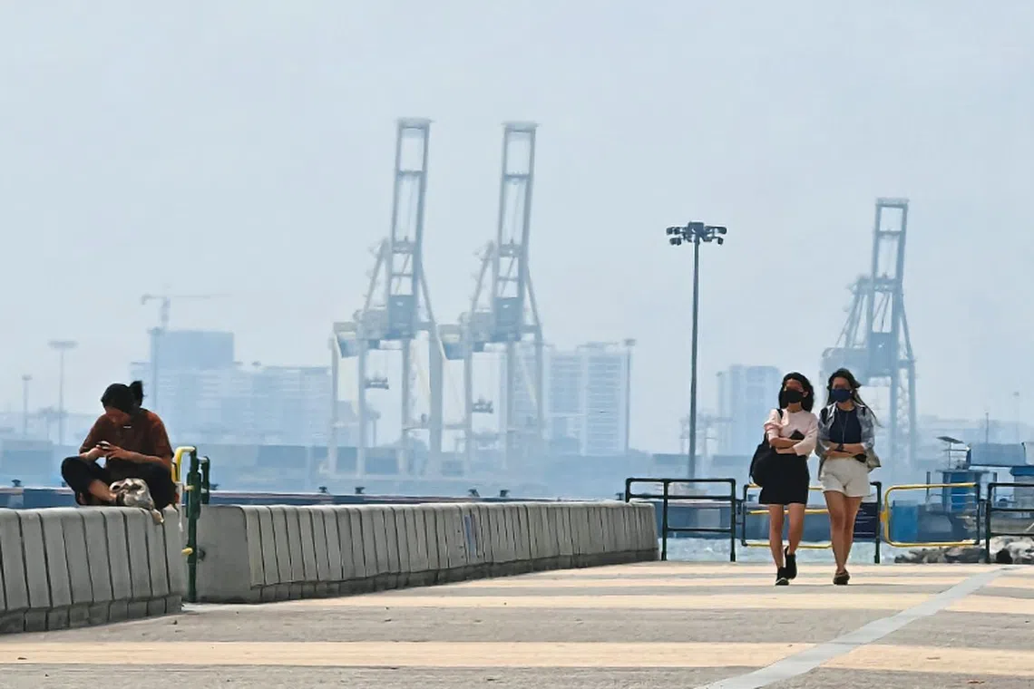 People walking along the Esplanade as the North Butterworth Container Terminal is shrouded in a blanket of haze in George Town, Penang.
