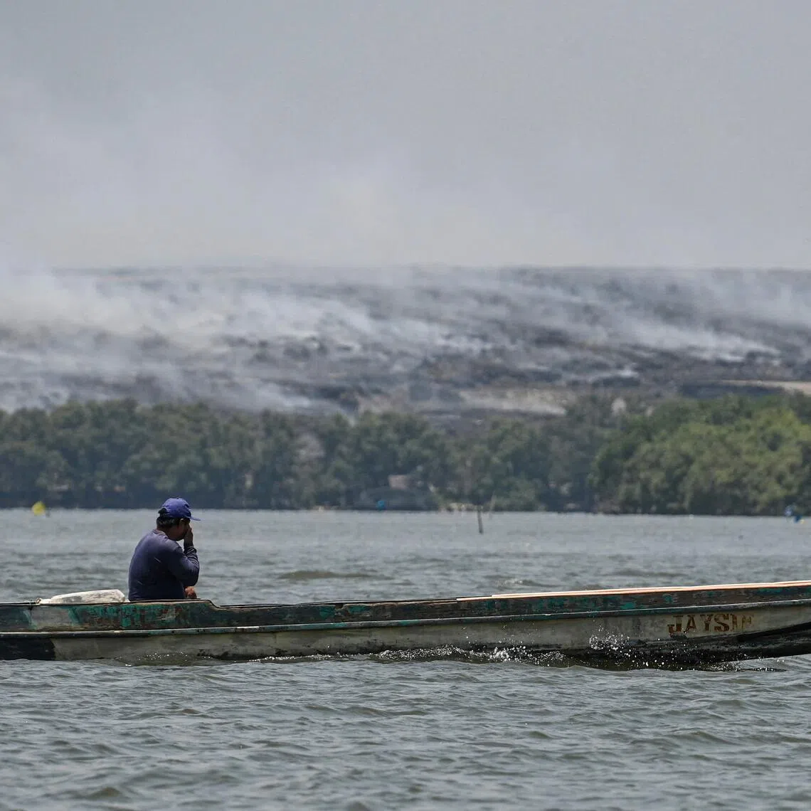 A boatman covers his face as he sails past grey smoke billowing from a burning landfill in the nearby Navotas City.