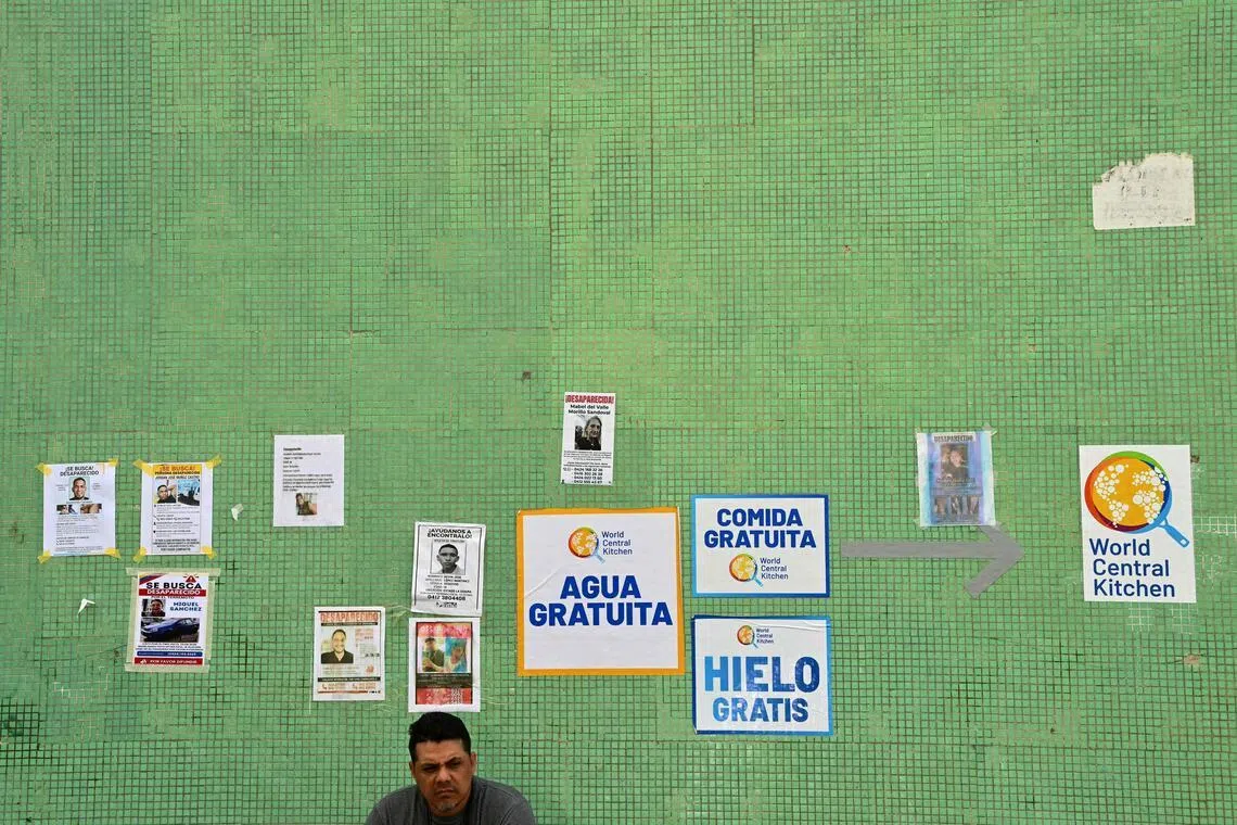 A man sits against a wall displaying signs with pictures and data of missing people and ads offering free food, ice, and water, in Caraballeda, state of La Guaira, Venezuela, on July 10.