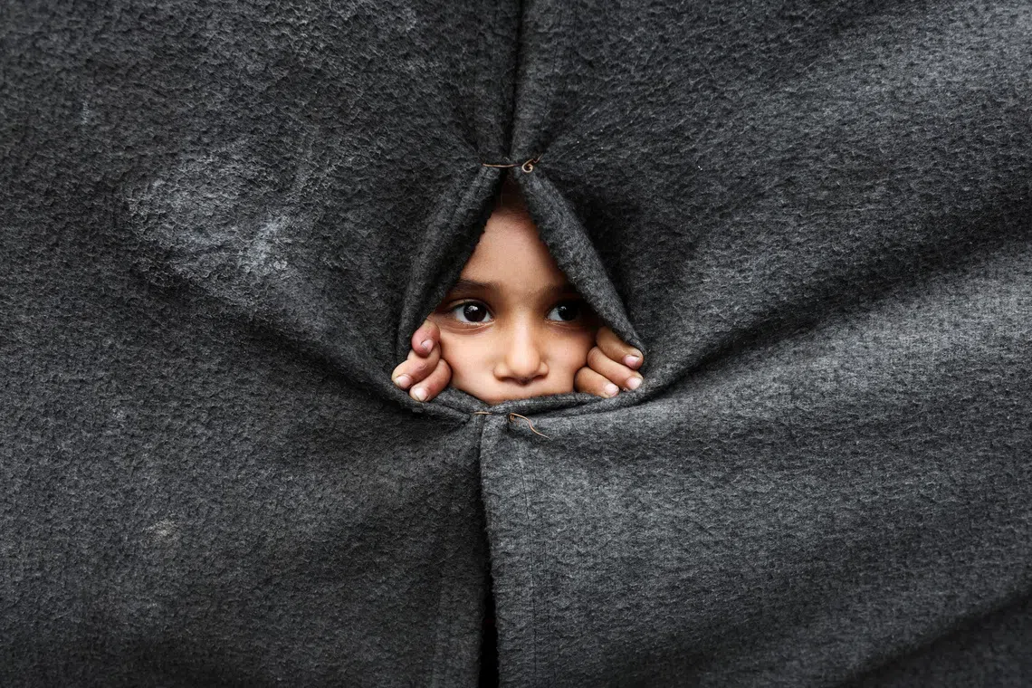 A displaced Palestinian child looking through a covering made from blankets as they take shelter at an UNRWA-run school, after U.S. President Donald Trump announced that Israel and Hamas agreed on the first phase of a Gaza ceasefire, in Khan Younis in the southern Gaza Strip, on Oct 9, 2025. 