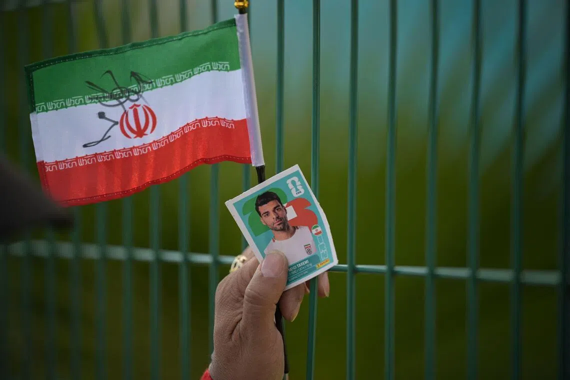 An Iran fan holding a flag and a Panini World Cup sticker of Iran’s forward Mehdi Taremi as the team’s players leave for the US at the Marriott Hotel in Tijuana, Mexico, on June 20, 2026, on the eve of their 2026 World Cup Group G match against Belgium.