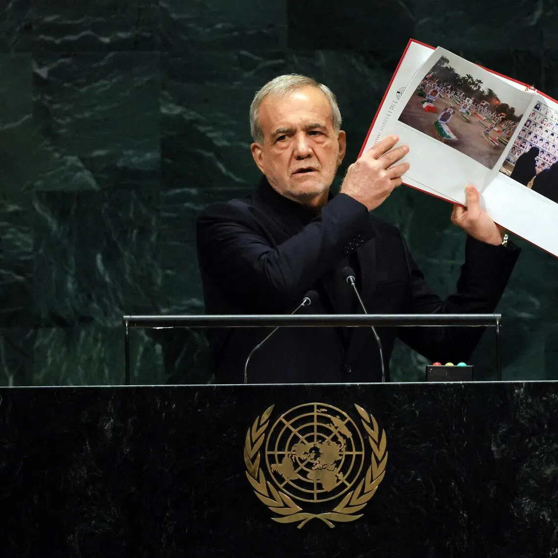 Iranian President Masoud Pezeshkian holds up pictures of alleged victims killed during the Israeli and American air strikes.