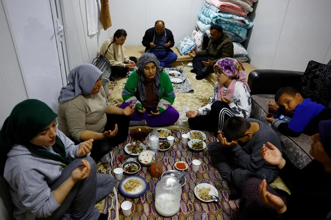 Members of the Arslan family pray at dinner in one of the three container homes where they live by a petrol station after losing their homes in the aftermath of a deadly earthquake in Nurdagi, Turkey, March 4, 2023. REUTERS/Susana Vera