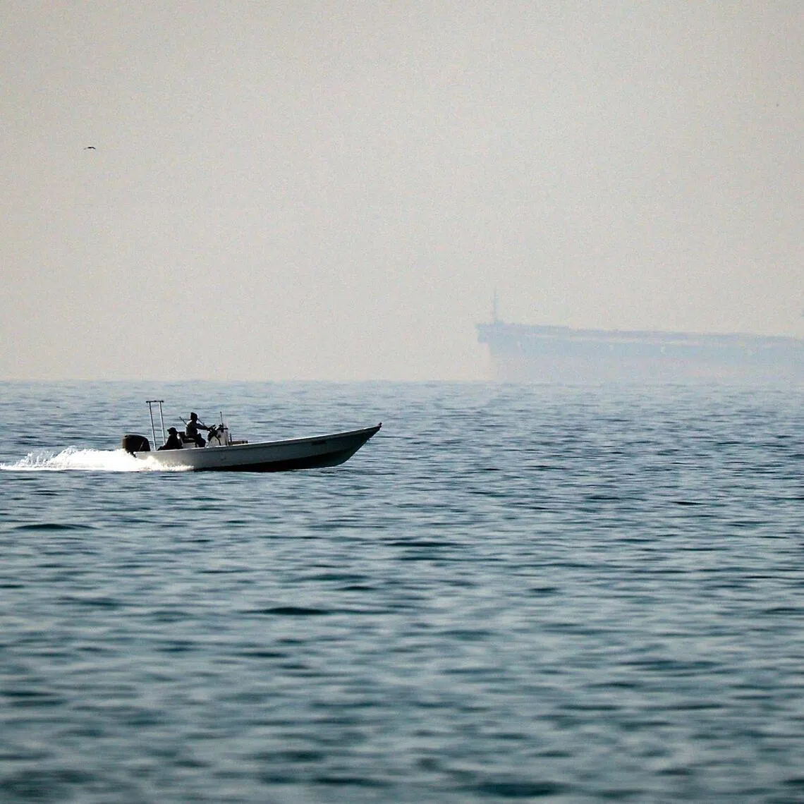 A motorboat cruises along off the town of Al Jeer on the Strait of Hormuz, with a tanker in the background, on Feb 25.