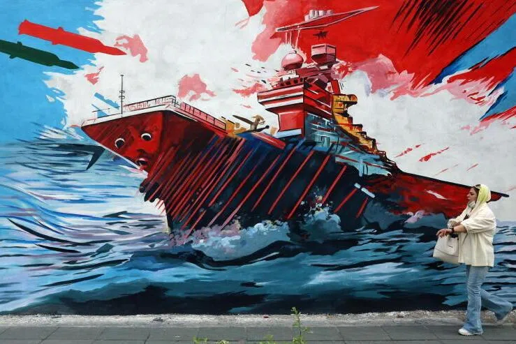 An Iranian woman walking past an anti-USA and anti-Israel mural on a street in Tehran. Iran has been using the Strait of Hormuz as a leverage in peace talks. 