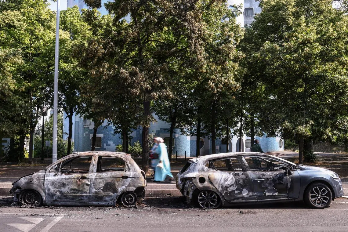 People walk past burnt out cars following a night of civil unrest, in Nanterre, near Paris.