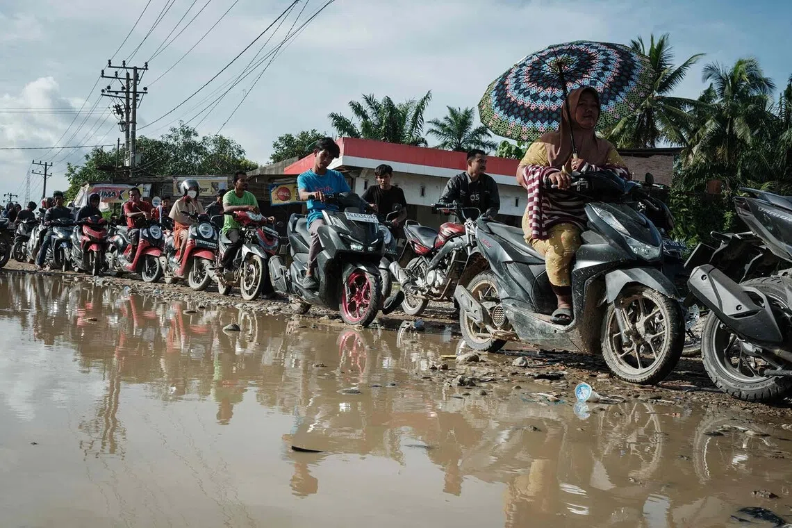 TOPSHOT - People wait in line for two hours to get fuel at a petrol station in an area where lifelines are still affected by a flash flood that occurred about three weeks ago in Aceh Tamiang, Northern Sumatra, on December 14, 2025. Devastating floods and landslides have killed 1,006 people in Indonesia, rescuers said on December 13 as the Southeast Asian nation grapples with the huge scale of relief efforts. (Photo by Yasuyoshi CHIBA / AFP)