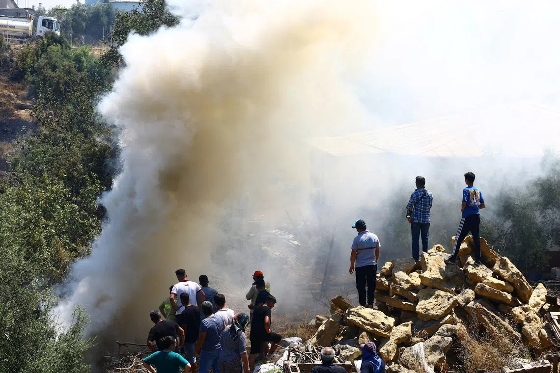 People stand next to smoke rising from the wildfire in the Aksu district of Antalya, a Mediterranean city in southern Turkey, July 25, 2025. REUTERS/Kaan Soyturk/File Photo