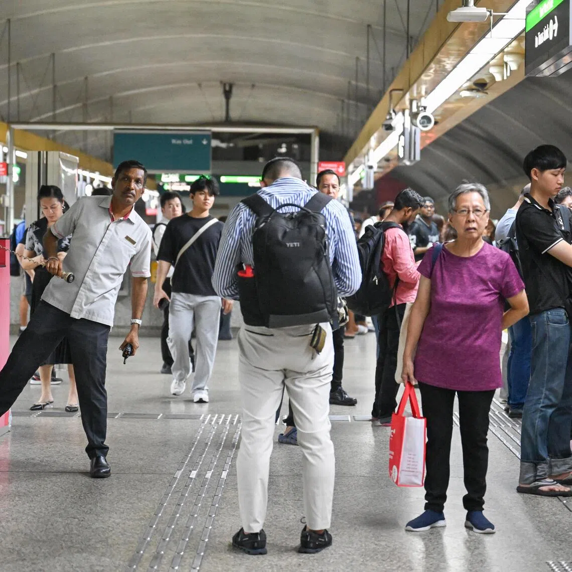 A train staff looking on, and commuters waiting for a train at Kallang MRT station, at 8.39pm, after the announcement of a train fault which had occured, on Dec 2, 2025.