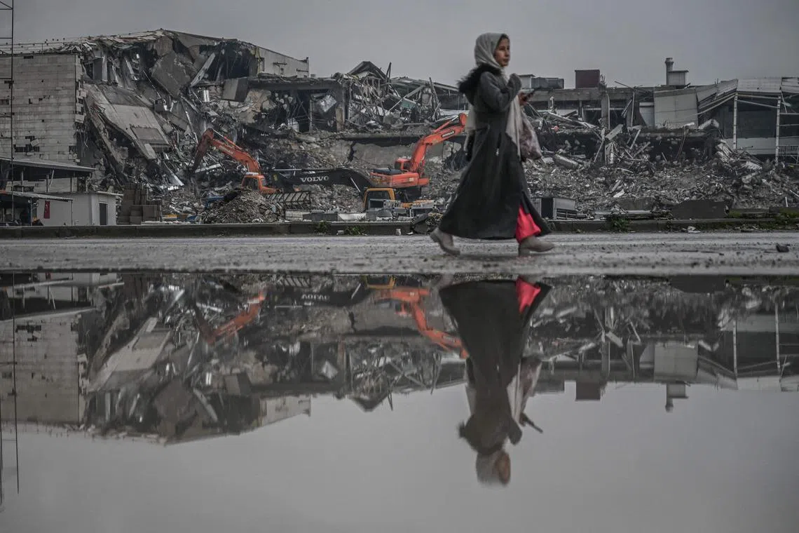 A woman walks past a flooded street as diggers work to clean the rubble of collapsed buildings eleven months after a 7.8-magnitude earthquake jolt and aftershocks wiped out swathes of Turkey's mountainous southeast, in Antakya on January 12, 2024. The double earthquake, in the middle of the night of February 6, 2023, killed more than 50,000 people and erased swathes of entire cities across Turkey's southeast. No place was affected more than Antakya -- a mountain-rimmed cradle of civilisations near the Syrian border where nearly 90 percent of the buildings were lost. (Photo by Ozan KOSE / AFP)
