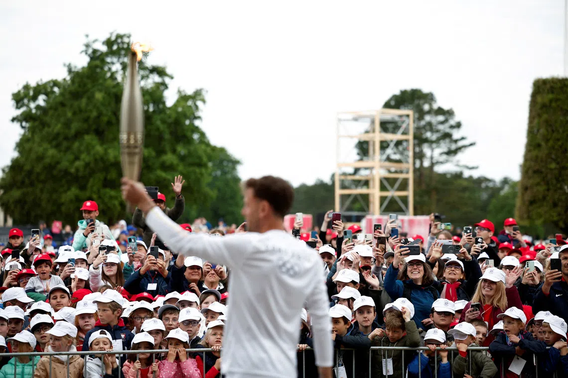 FILE PHOTO: People take photos as torchbearer Nicolas-Marie Daru holds the Olympics torch during the relay ahead of the Paris 2024 Olympic games, at the World War II Normandy American Cemetery and Memorial, in Colleville-sur-Mer, situated above Omaha Beach, Normandy region, France, May 30, 2024. REUTERS/Benoit Tessier/File Photo