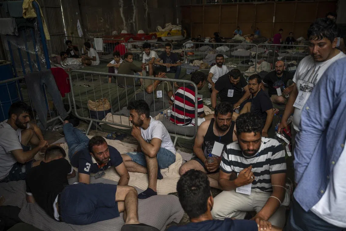 Survivors of the shipwreck sit inside warehouse in Pylos after being rescued.