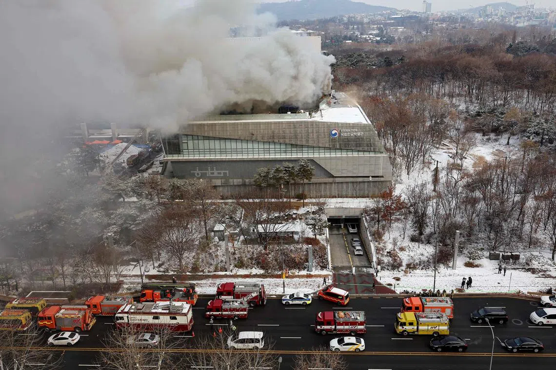 Fire engines are seen on a road as smoke rises from the roof of the National Hangeul Museum in Seoul on February 1, 2025. (Photo by YONHAP / AFP) / - South Korea OUT / NO ARCHIVE /  REPUBLIC OF KOREA OUT  / NO ARCHIVES -  RESTRICTED TO SUBSCRIPTION USE