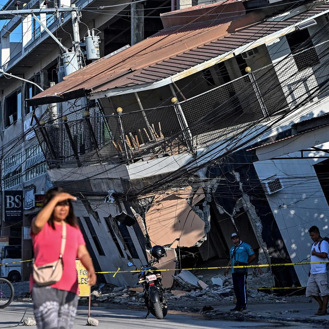 A woman walks past a collapsed building a day after the magnitude 7.8 earthquake, in Calumpang, General Santos, in Philippines.