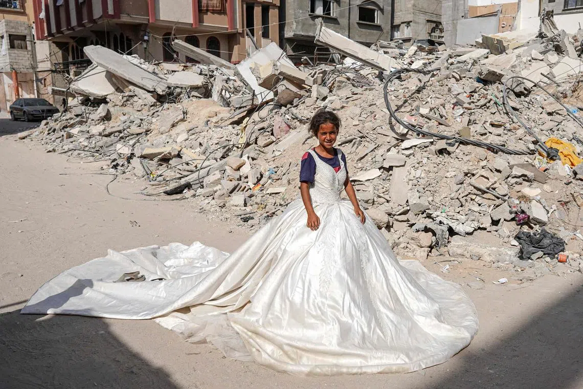 A Palestinian girl posing with a wedding dress found amid the rubble of buildings destroyed during Israeli bombardment, in Khan Yunis in the southern Gaza Strip, on June 20, 2024.