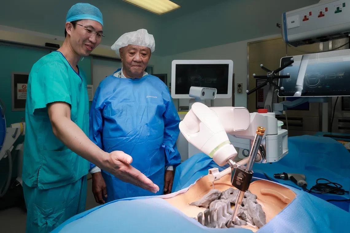 A/Prof Jacob Oh, Head and Senior Consultant of Spine Service TTSH, Director of NHG Spine Centre, President-Elect of Singapore Spine Society, with his former patient Mr Ng Beng Piau, 85, in a TTSH operating theatre on July 16, 2024. Dr Oh is demonstrating the Robot-Assisted Spine Technology on a mannequin. 