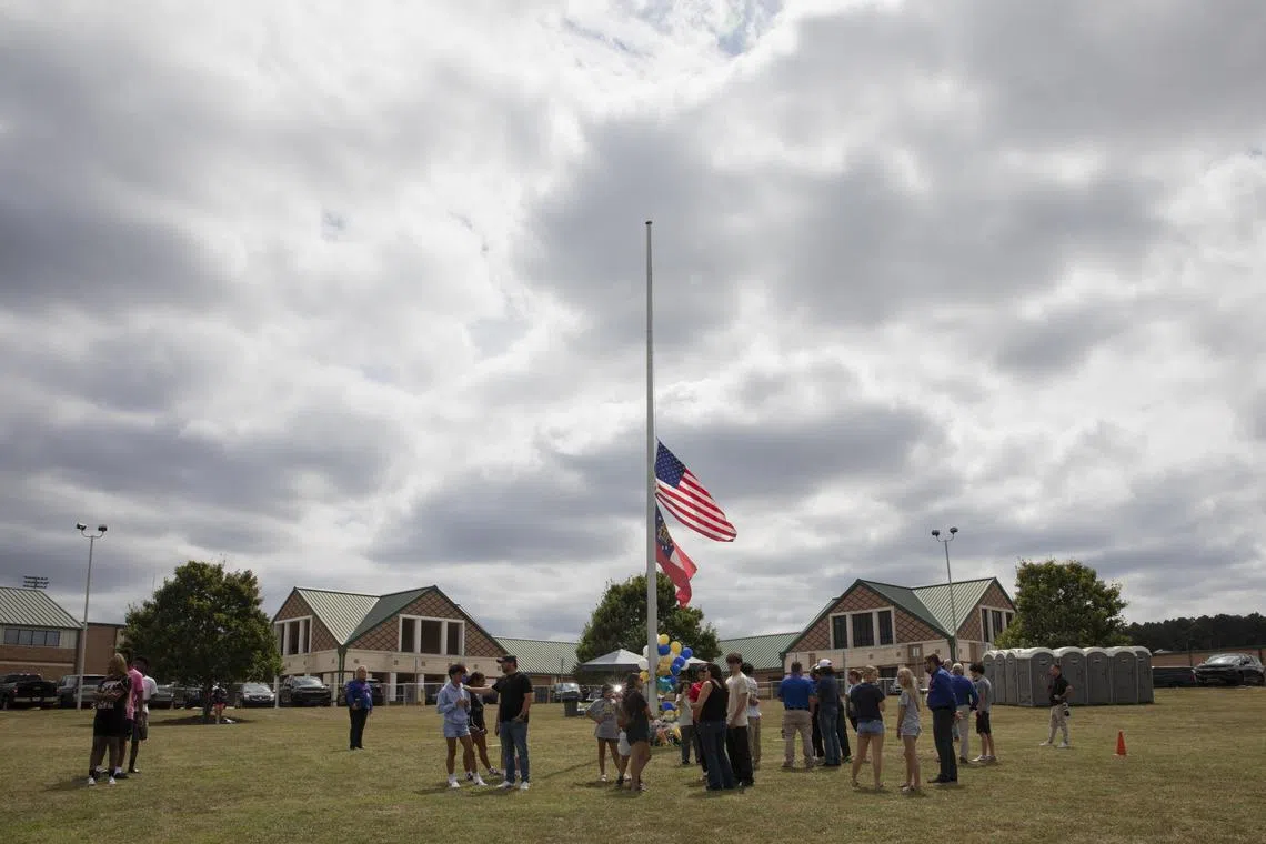People gather at a makeshift memorial at the flagpole, where the flags were flying at half staff, outside Apalachee High School in Winder, Ga., Sept. 5, 2024. A 14-year-old is accused of killing two students and two teachers with a military-style rifle at Apalachee High School in Winder on Wednesday morning. Eight students and a teacher were injured. (Amanda Kathleen Greene/The New York Times)
