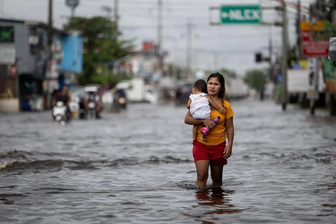 A woman carrying a baby wades through a flooded area in Manila North Road following heavy rains brought by Typhoon Co-may in Minalin, Pampanga, Philippines, July 25, 2025. REUTERS/Eloisa Lopez
