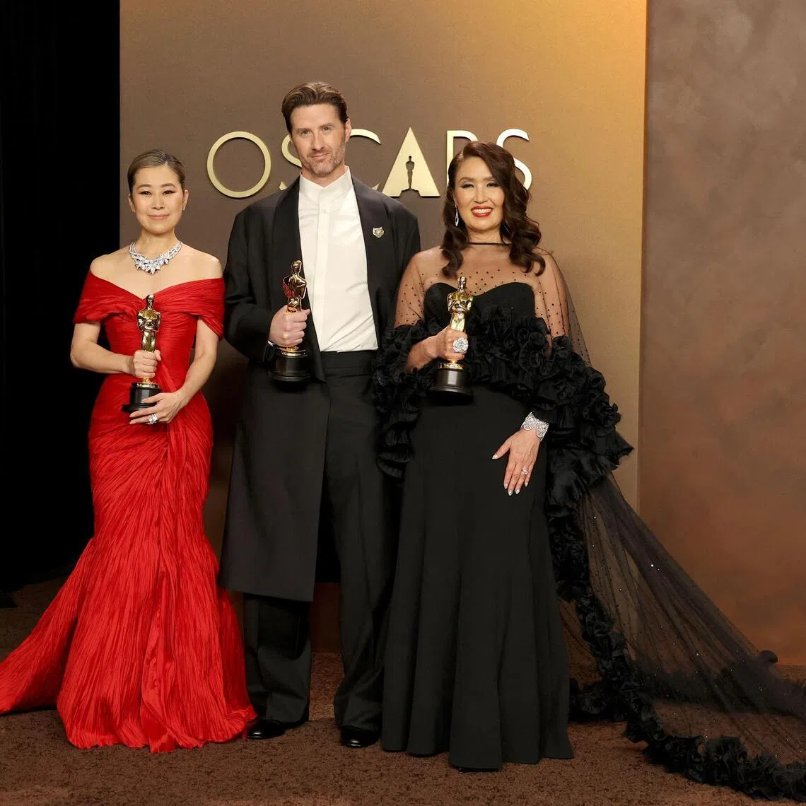 (From left) Maggie Kang, Chris Appelhans, and Michelle L.M. Wong, winners of the Best Animated Feature Film Award for KPop Demon Hunters, pose in the press room during the 98th Oscars at Dolby Theatre on March 15.