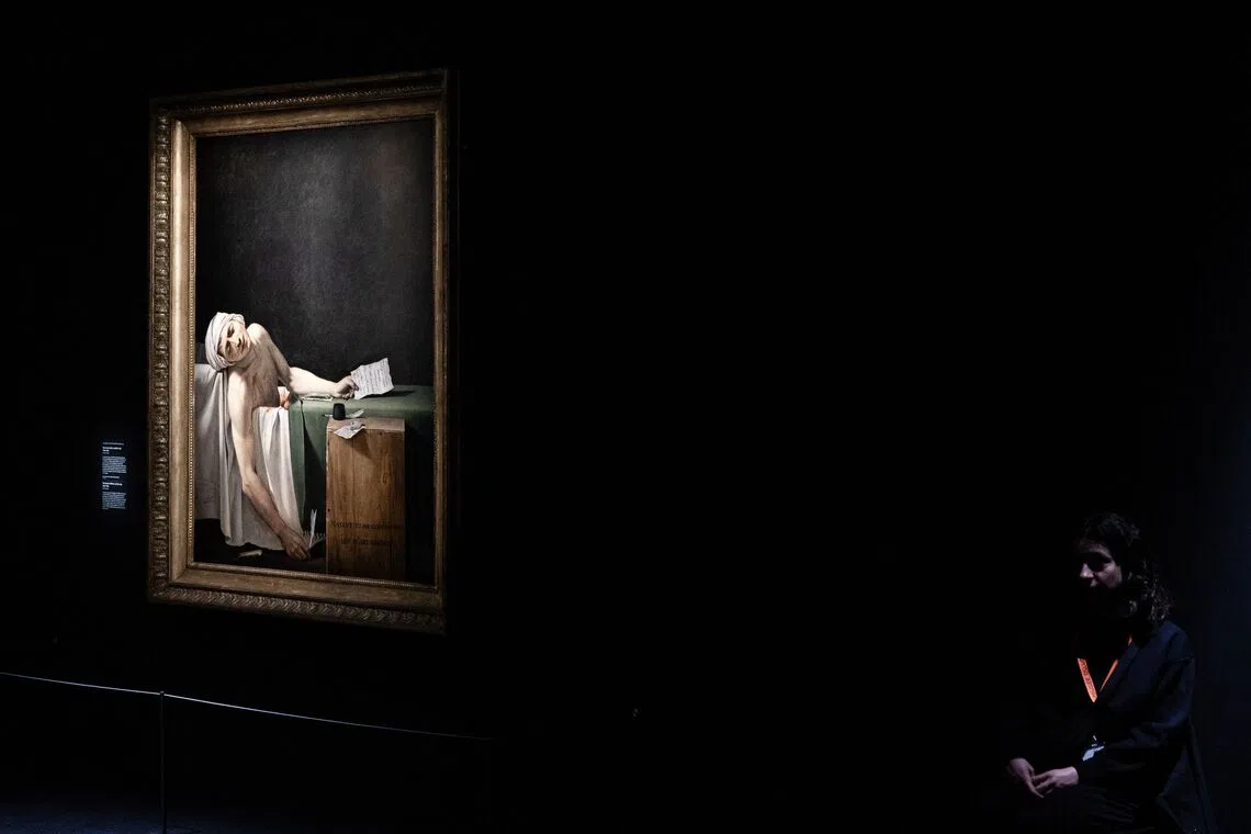 A museum staff sitting by the painting "The death of Marat" by late French artist Jacques-Louis David, at the Louvre museum, in Paris, on Oct 14, 2025, on the eve of the opening of the exhibition "Jacques-Louis David". 