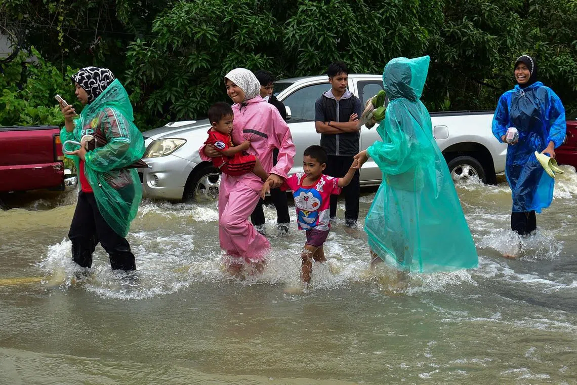 Women wear rain ponchos as they walk with children through floodwaters following heavy rain in Thailand's southern province of Narathiwat on December 25, 2023. Floods caused by intense rainfall have affected tens of thousands of people in Thailand's deep south, officials said December 25, with some roads and railway lines forced to close. (Photo by Madaree TOHLALA / AFP)
