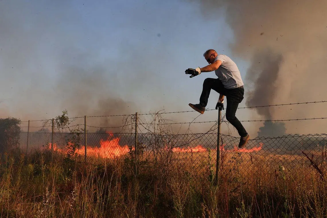 A man jumping over a fence as flames and smoke rises from a wildfire in a village in Dubrava, Kosovo, July 22, 2025.