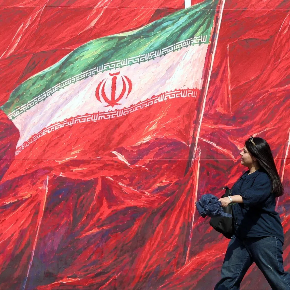 An Iranian woman walking past a banner in Tehran on Oct 14 featuring Iran’s national flag.