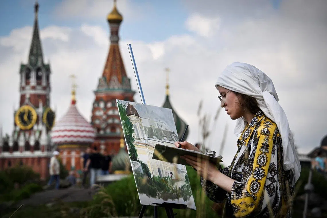 A girl painting in front of the Kremlin's Spasskaya tower and St. Basil's cathedral in downtown Moscow on July 23, 2025. 