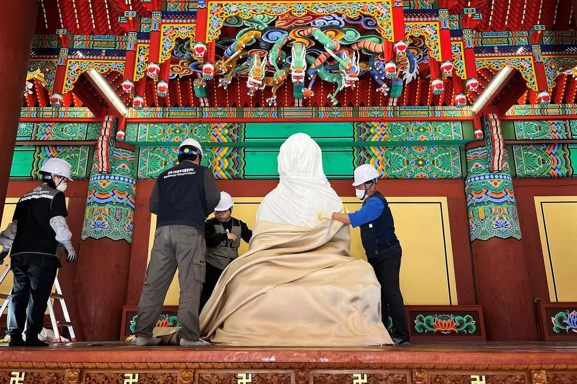 Officials wrapping a Buddha statue with a fire-retardant blanket to protect it from a wildfire at Gounsa temple in Uiseong, South Korea, on March 25, 2025. 