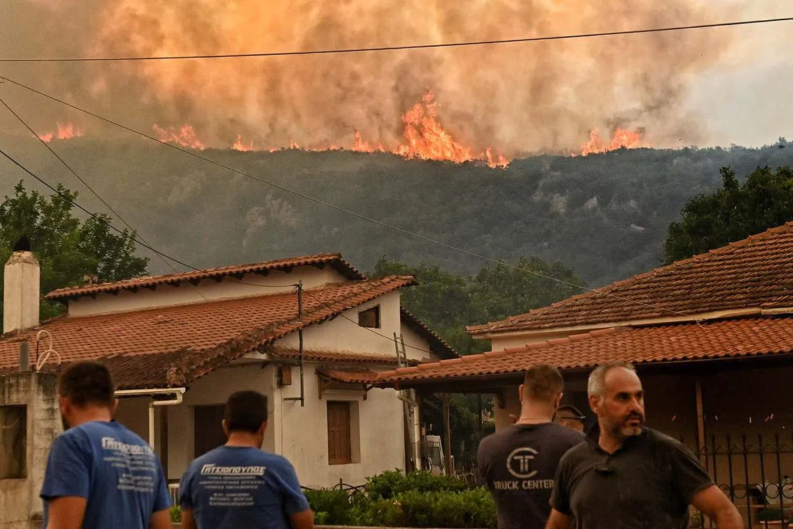 Residents watching flames rising from a wildfire burning next to the village of Karteri, in Feneos area, near Corinth, Greece, July 22, 2025. 