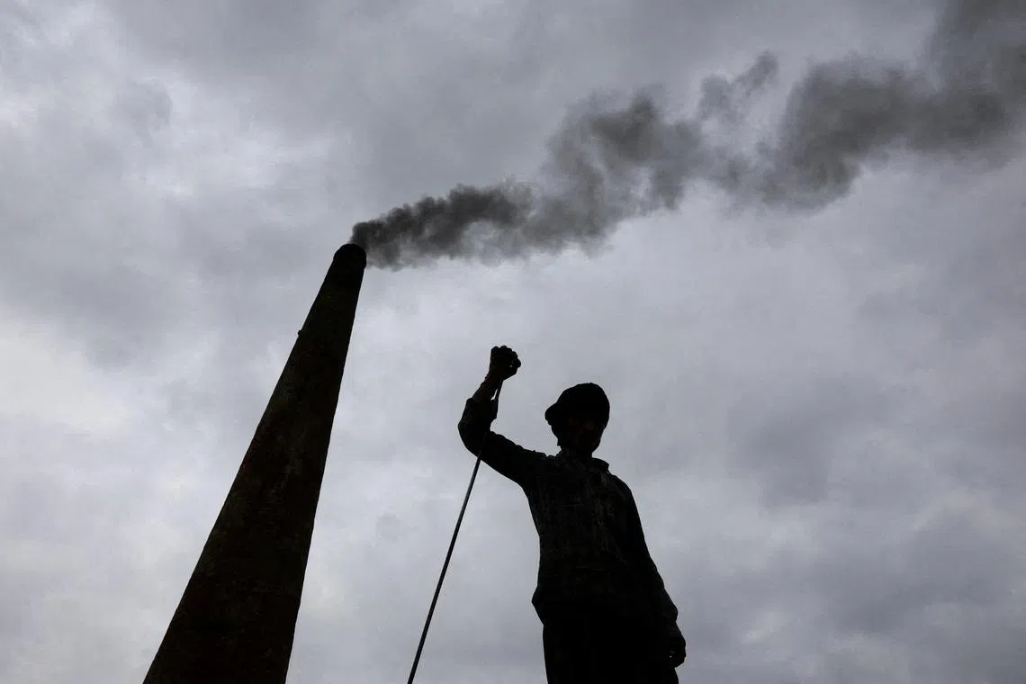 A worker standing as smoke rises from a chimney at a brick kiln, in Mathura, India, on June 19, 2025.