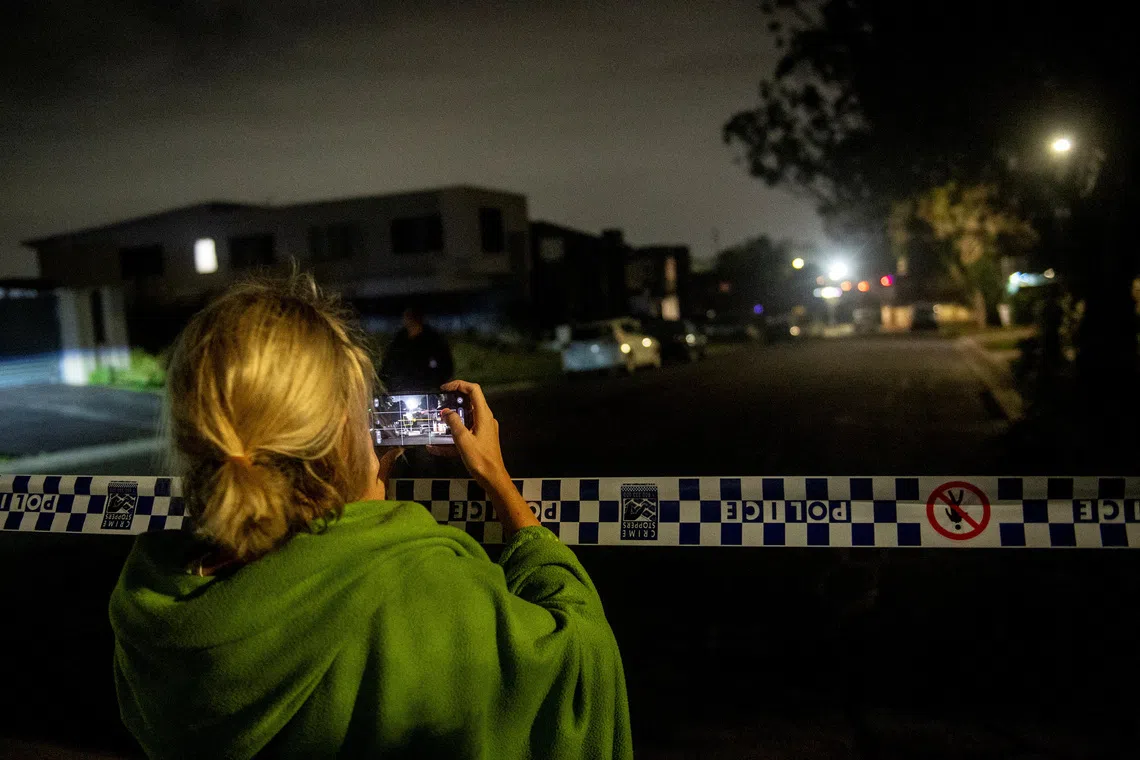 A woman records on her mobile phone as a police crime scene is established at the home of a suspect in Bonnyrigg, following a deadly shooting at Bondi Beach, on Dec 14.