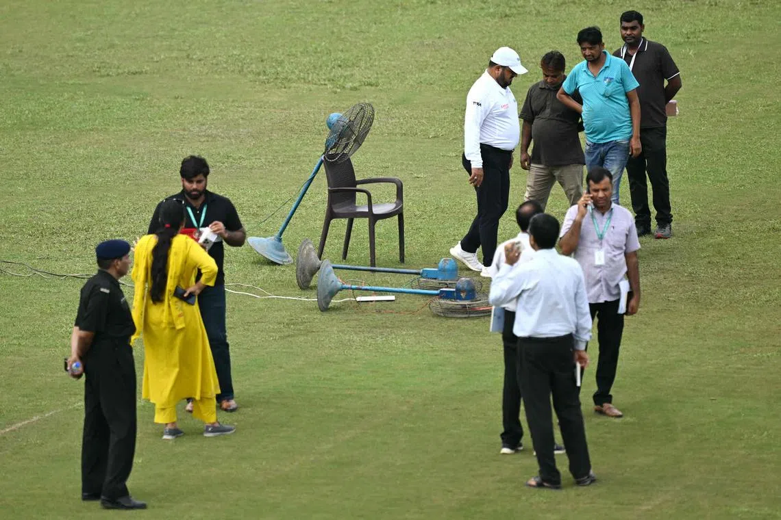 Groundsmen use fans to dry a patch of wet outfield as an official watches at the Shaheed Vijay Singh Pathik Sports Complex in Greater Noida, India on Sept 10, 2024. The one-off cricket Test between Afghanistan and New Zealand had yet to get under way after two days.