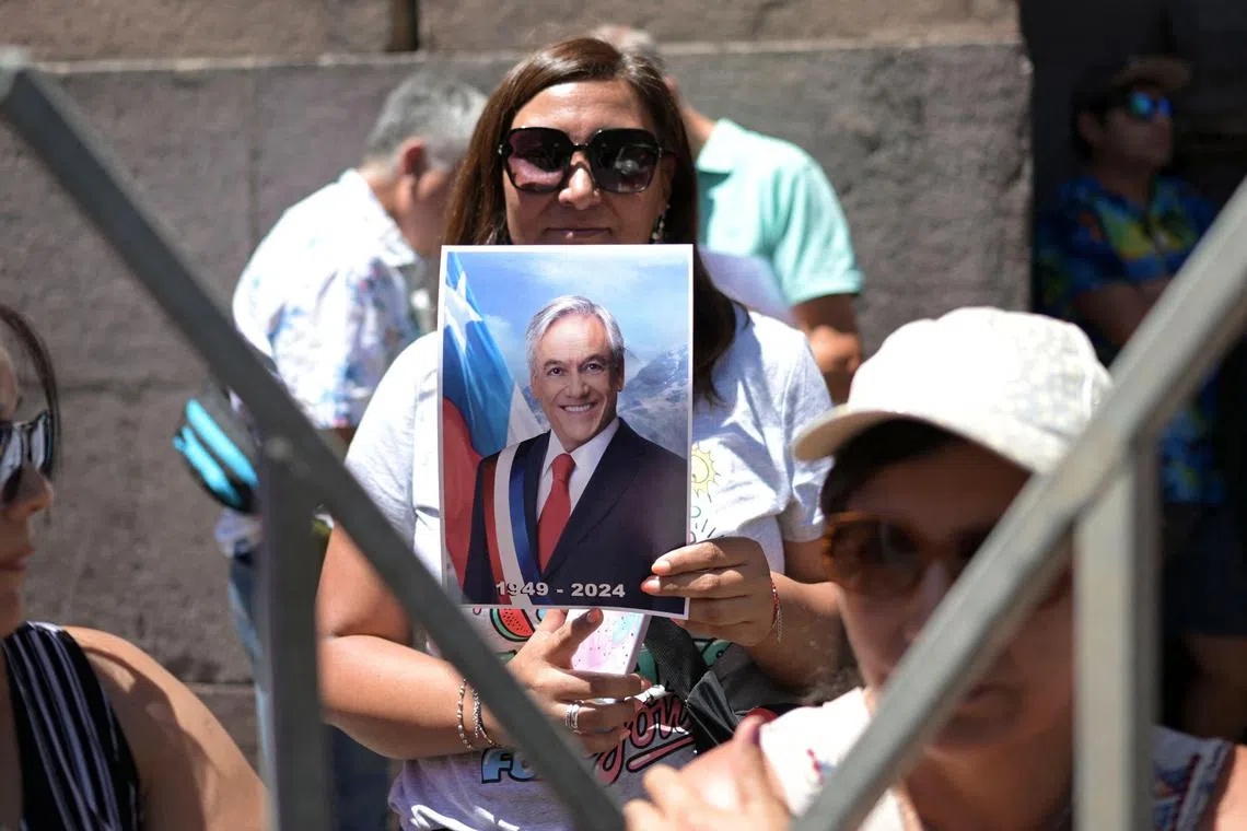 A supporter of the late former Chilean President Sebastian Piñera holds a picture of him as she waits to enter the National Congress Palace in Santiago on February 7, 2024. Three days of mourning and funeral ceremonies got underway Wednesday for Chile's ex-president Sebastian Pinera, who died a day earlier when the helicopter he was piloting crashed into a lake. (Photo by RODRIGO ARANGUA / AFP)
